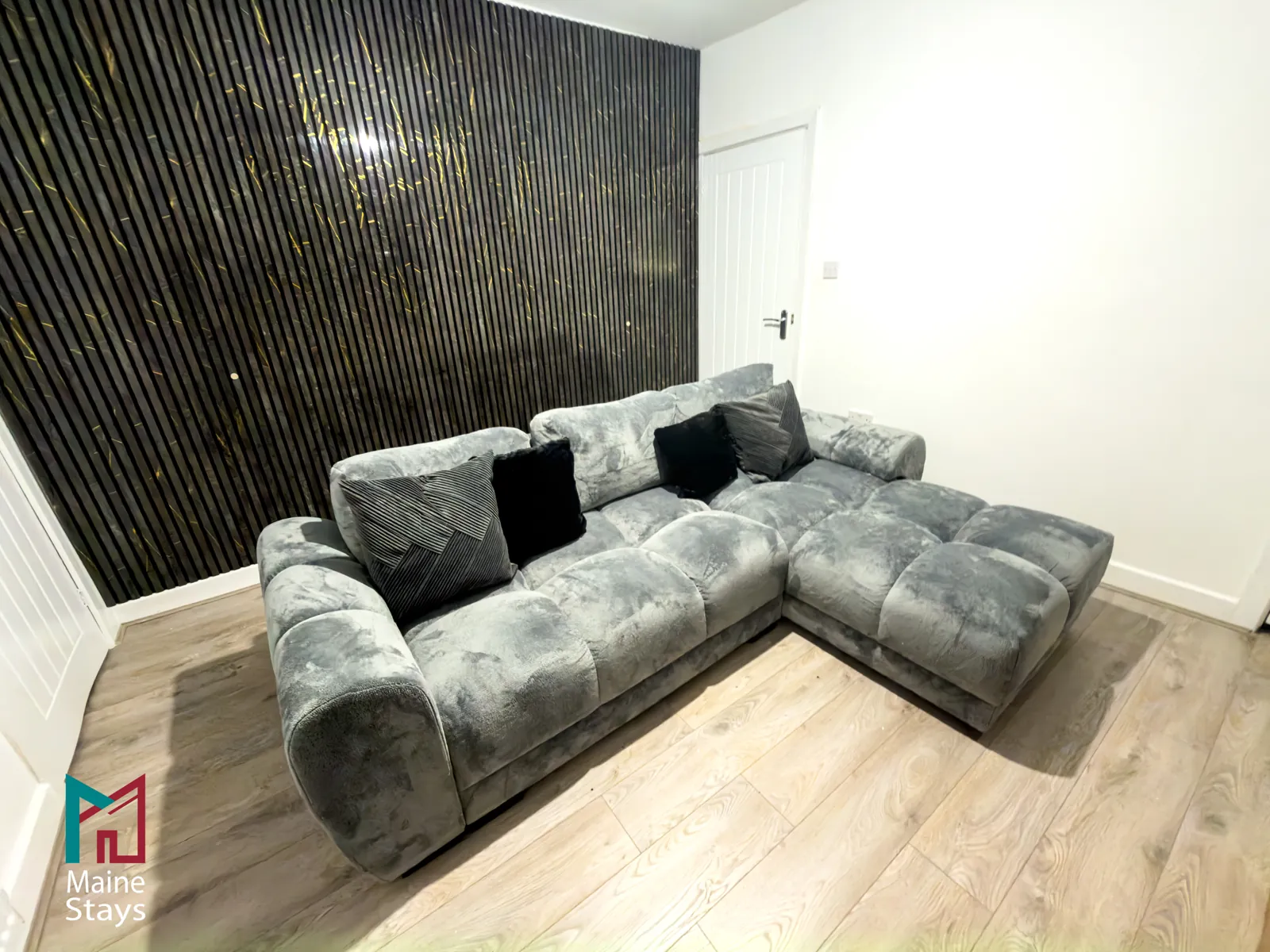 The Dudley Lounge — Living room with a large corner sofa and a black and gold feature wall