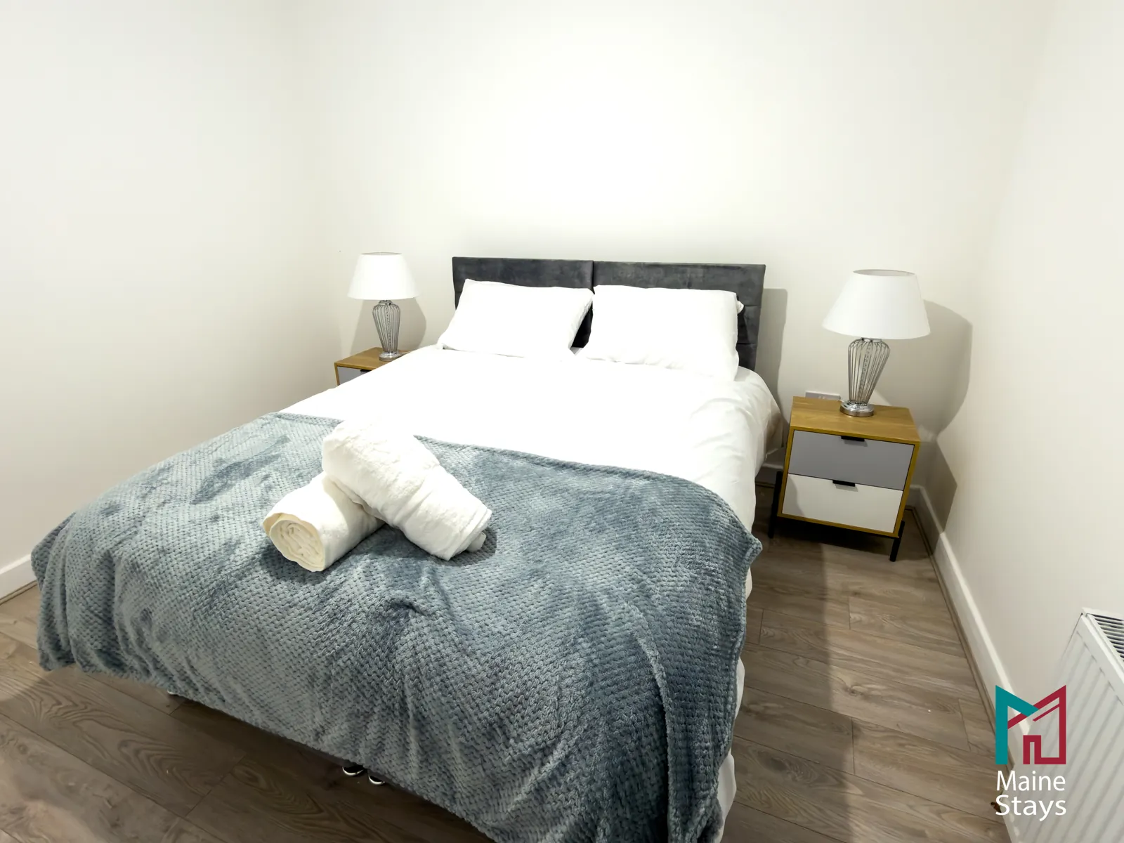The Dudley Lounge — Double bed with grey throw, towels and two bedside lamps