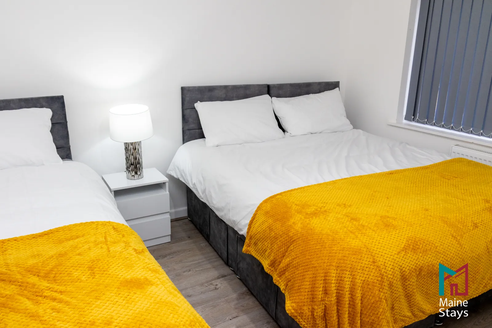 The Dudley Lounge — Double and single beds with mustard throws and a bedside lamp